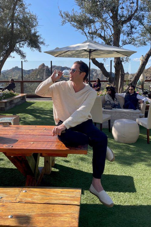 Josh Flagg sitting on picnic bench sipping a glass of wine